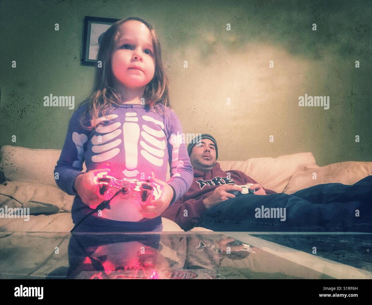 Petite fille en violet squelette pajamas holding controller à jouer à des jeux vidéo avec son père Banque D'Images