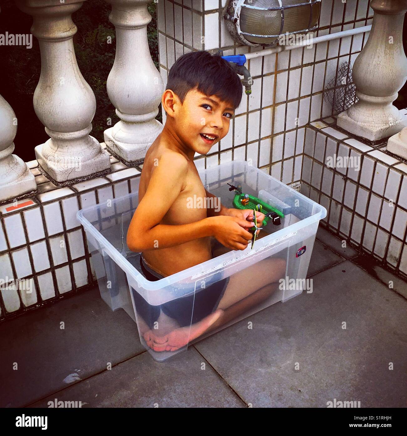 Jeune garçon dans une boîte en plastique transparent comme une piscine Banque D'Images