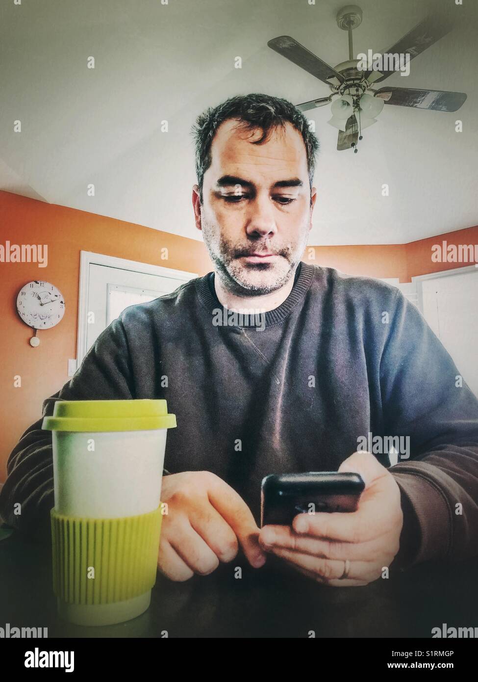 Homme de 40 ans non rasé lisant des articles de presse sur son smartphone tout en buvant un café dans sa cuisine - Image de stock capturée avec un smartphone