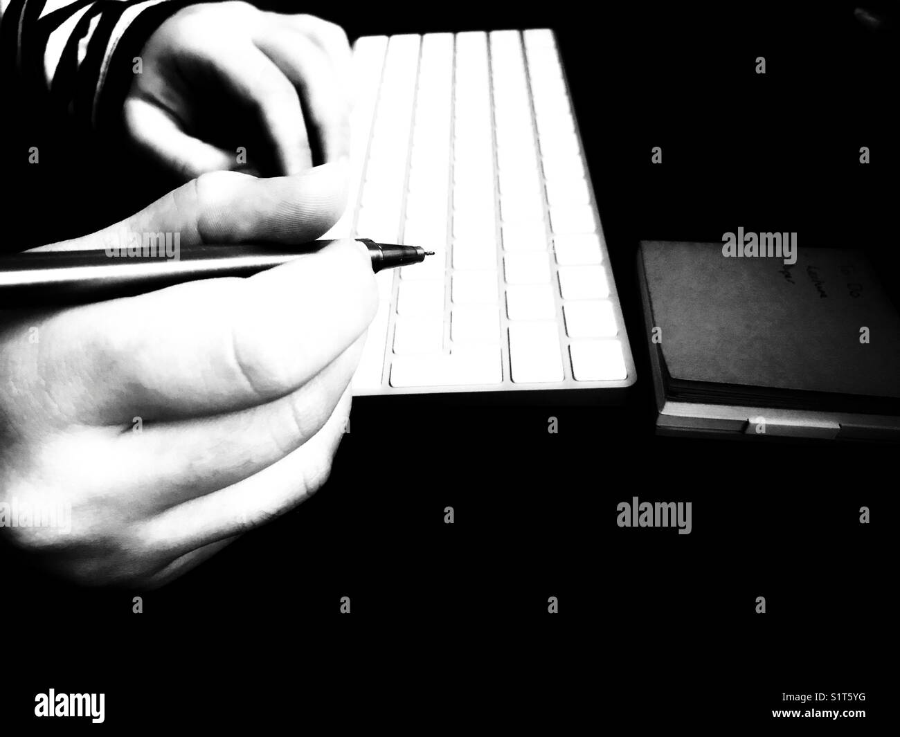 Mains de femme millénaire, tenant un stylo avec un clavier d'ordinateur et un bloc-notes sur le bureau supérieur en cuir. - Image de stock capturée avec un smartphone