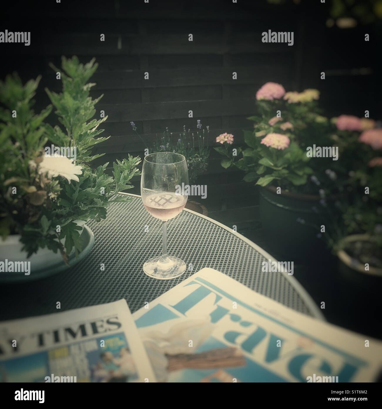 Un verre de vin et un journal section Voyages supplément sur une table de jardin, UK Banque D'Images