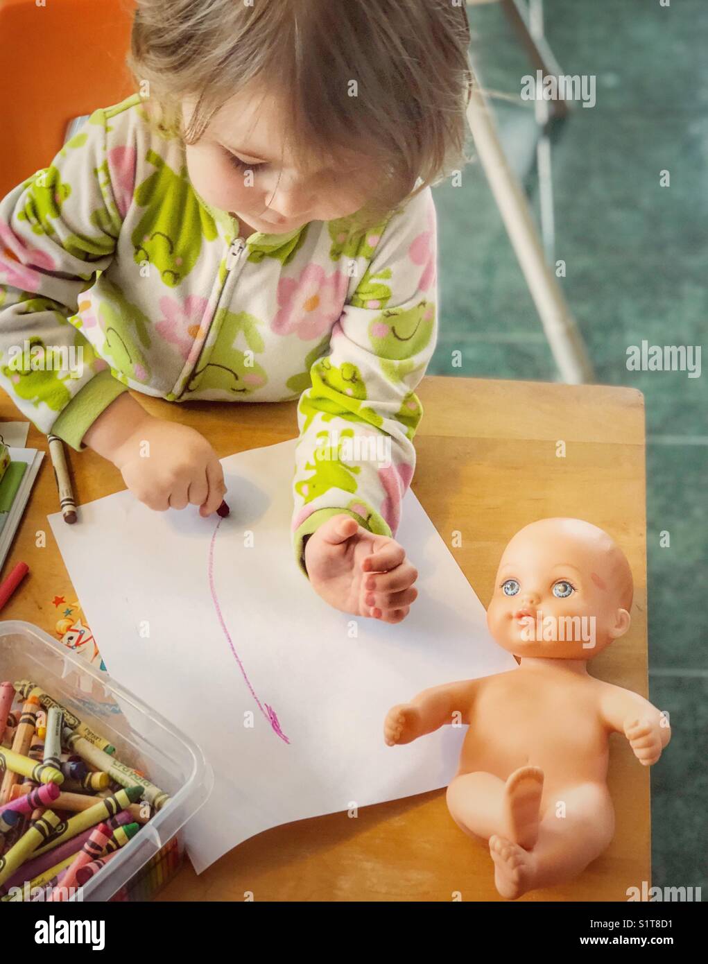 Coloriage bébé fille avec un crayon sur une table en bois avec une poupée sur elle Banque D'Images