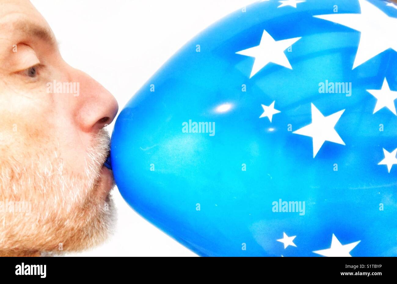 Homme d'âge moyen d'exploser un ballon bleu avec motif en étoile Banque D'Images