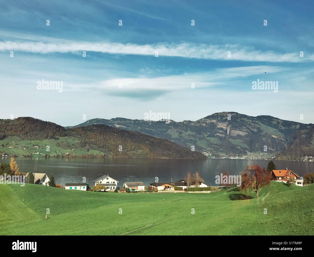Champ vert, maisons, lac, montagne et vue sur le ciel bleu Banque D'Images
