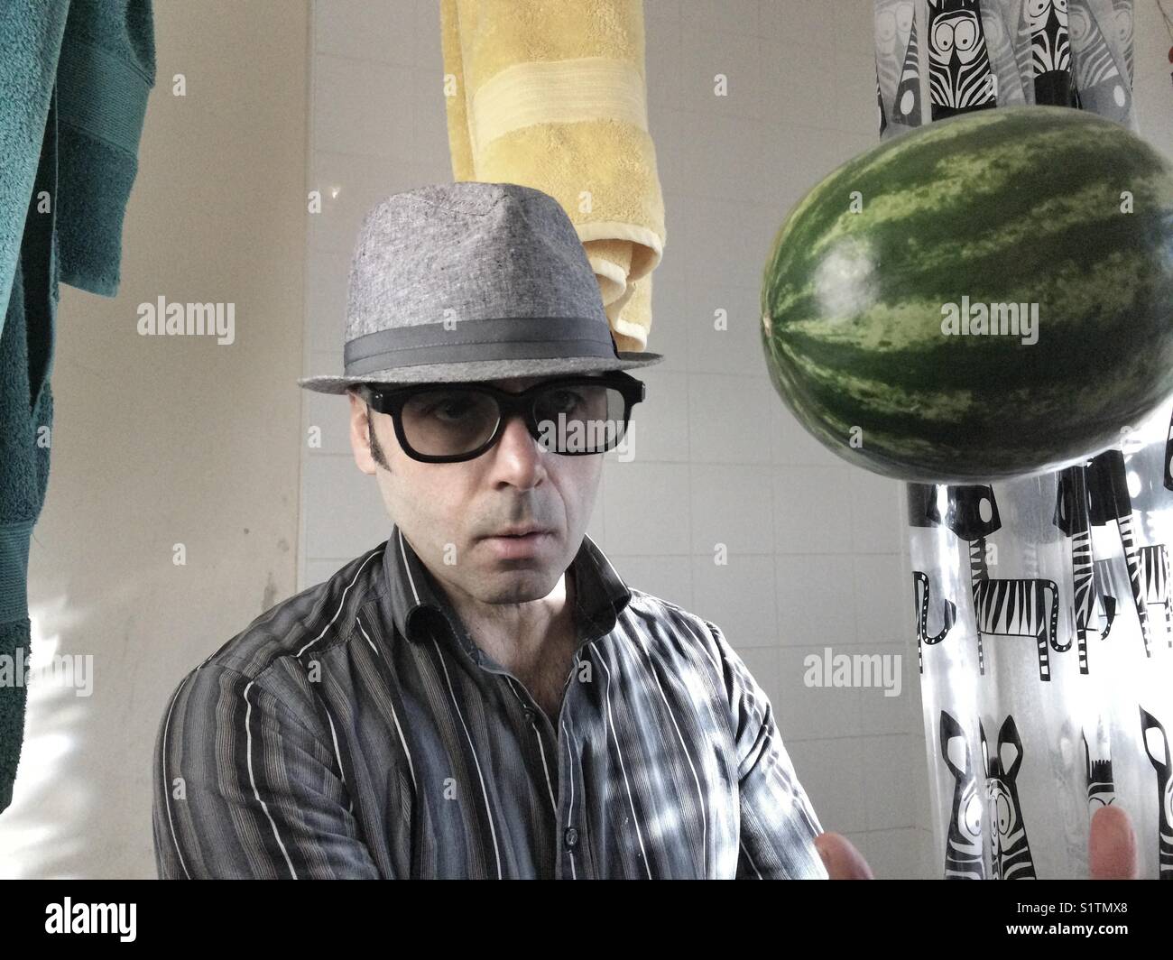 Portrait d'un homme avec des lunettes noires et un chapeau dans les toilettes avec le melon d'eau dans l'air Banque D'Images