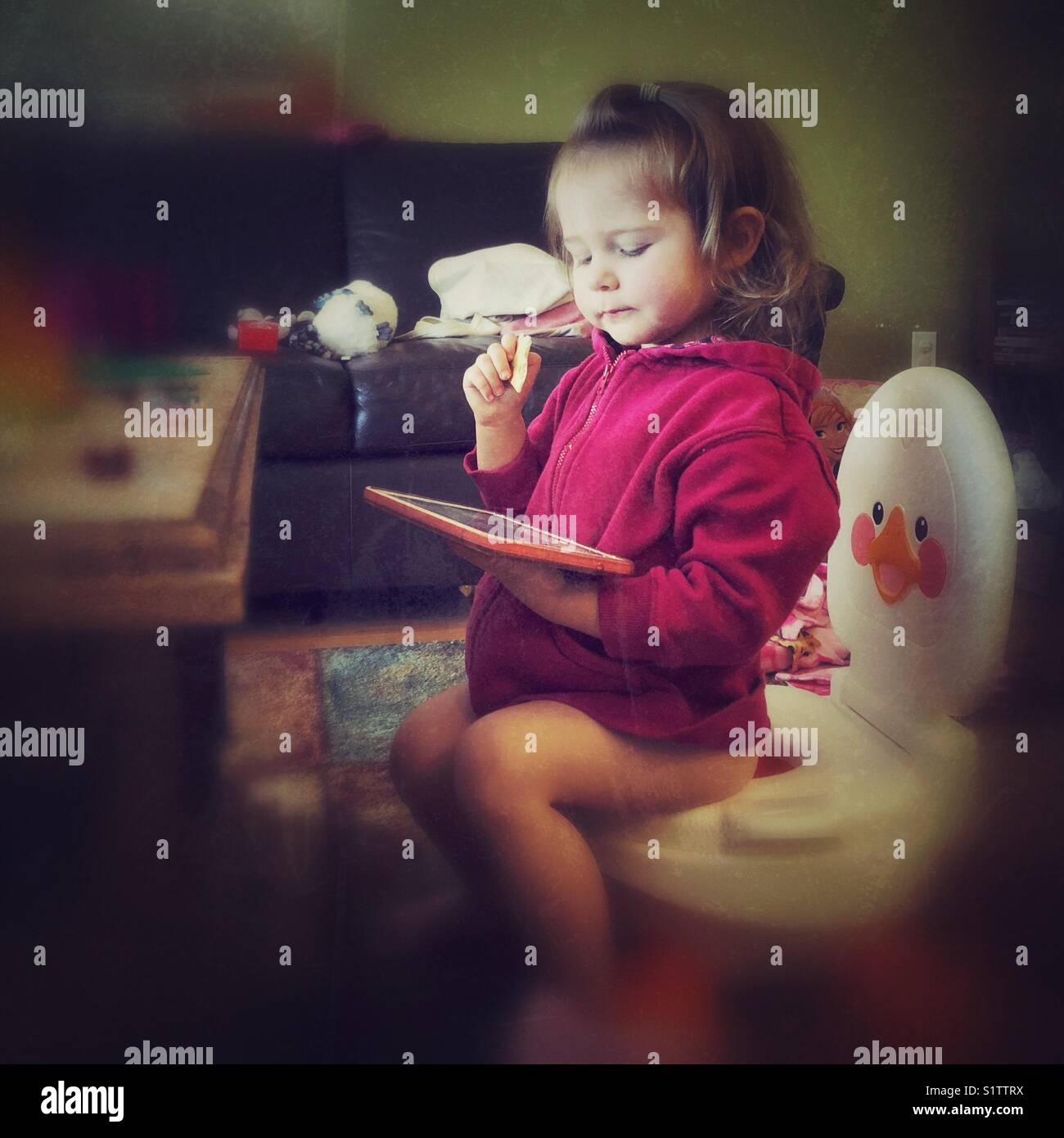 Formation toilettes bébé fille assise sur un pot dans une chambre familiale avec le comprimé dans une main et dans l'autre main craquelins Banque D'Images