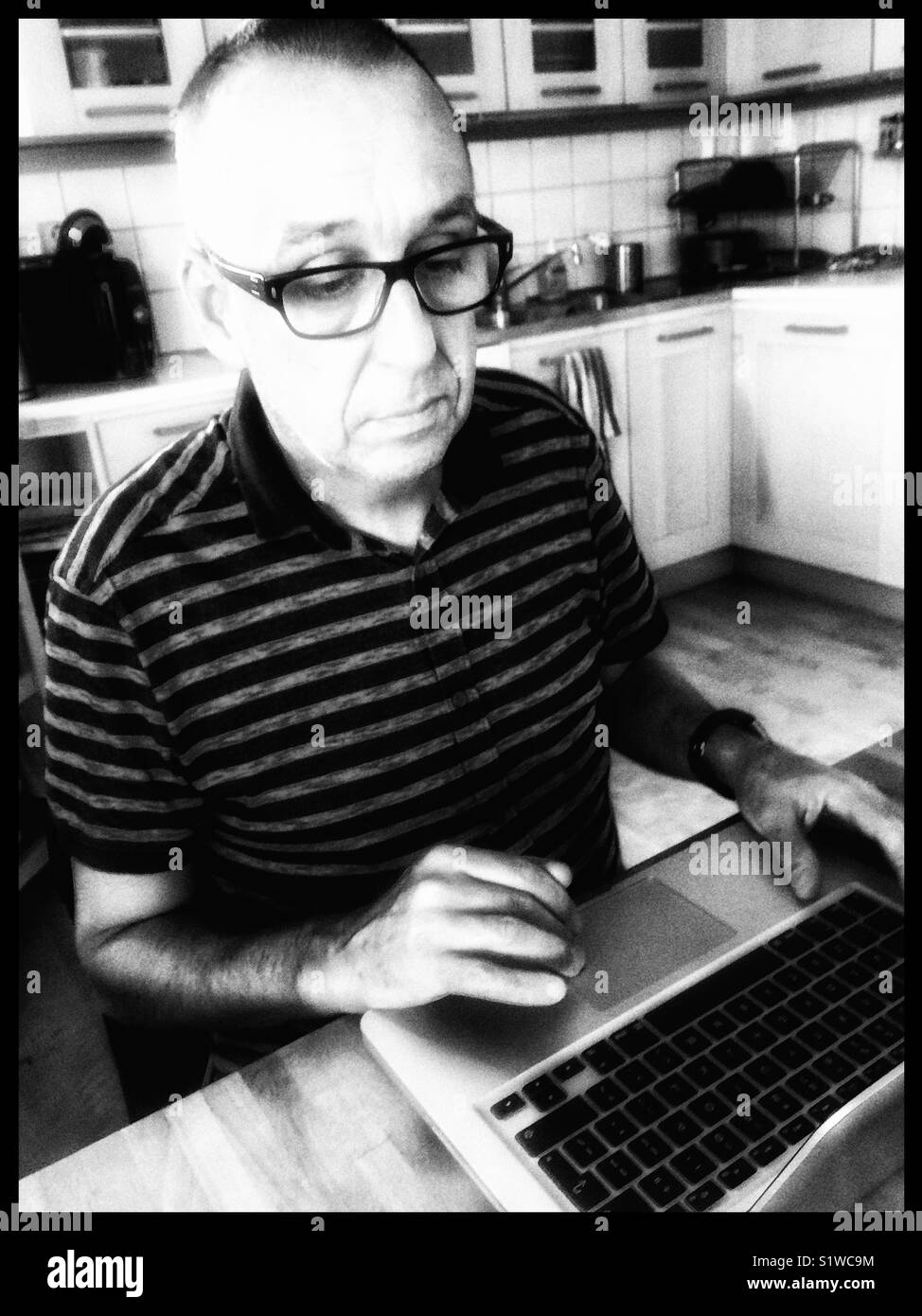 Homme d'âge moyen sérieux travaillant sur ordinateur portable dans la cuisine à la maison, la Suède Banque D'Images