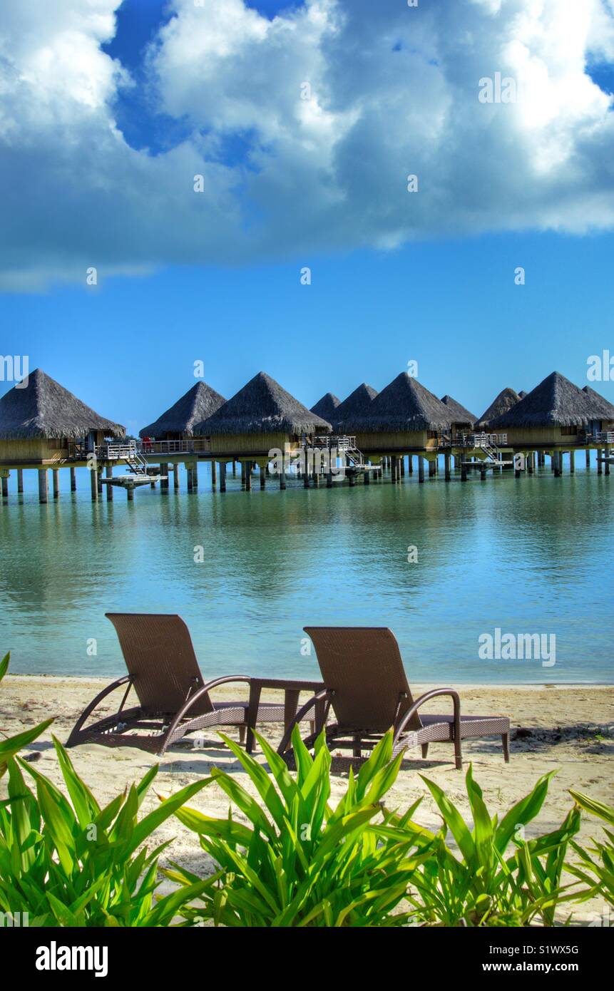 Des chaises longues sur la plage de Bora Bora, Polynésie française dans le Pacifique Sud. Bungalows sur l'eau utilisée par les jeunes mariés dans l'arrière-plan Banque D'Images
