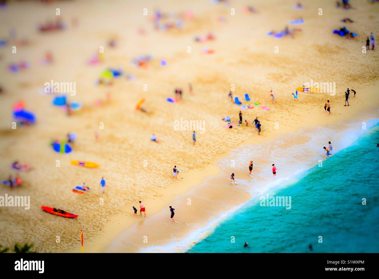 Une vue aérienne d'une longue plage de sable pendant les vacances d'été montrant les familles et amis jouant, le surf et la natation dans l'océan vert émeraude, d'en haut. Banque D'Images