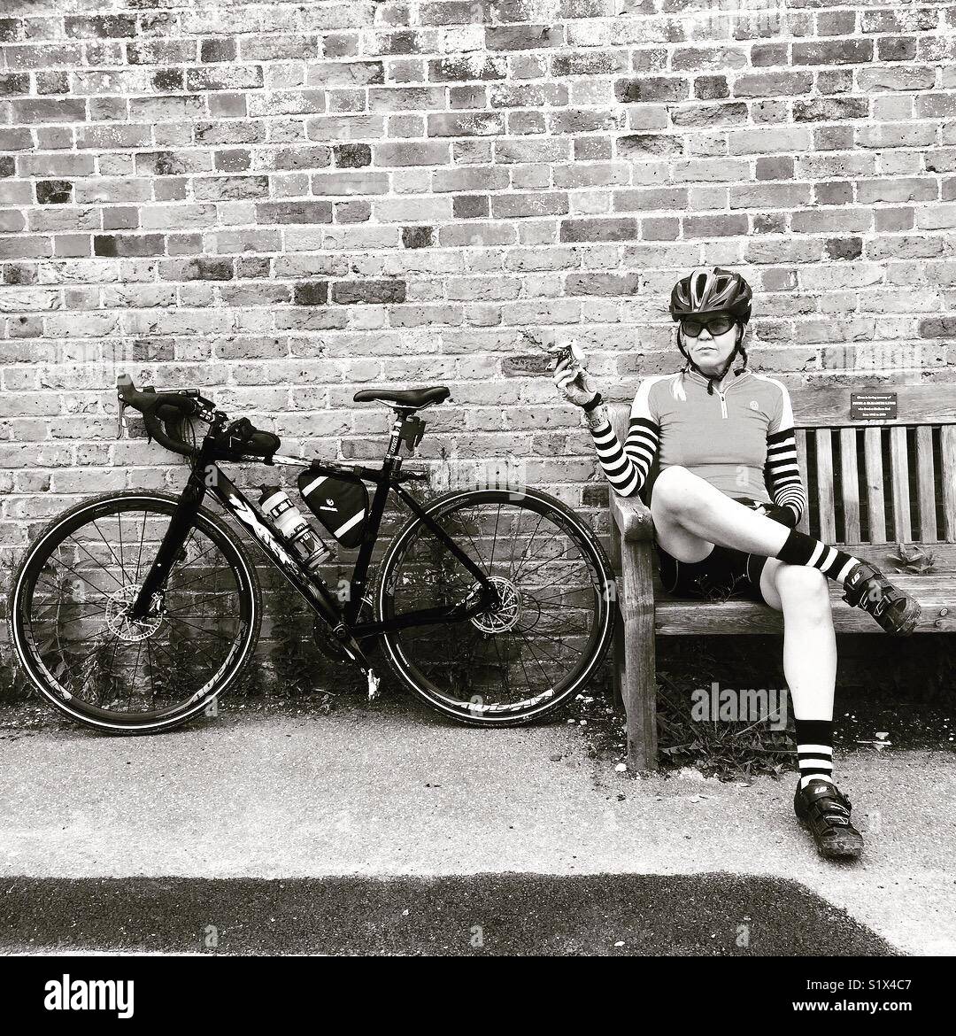 Un cycliste féminin prend une pause sur un banc avec son vélo à proximité Banque D'Images