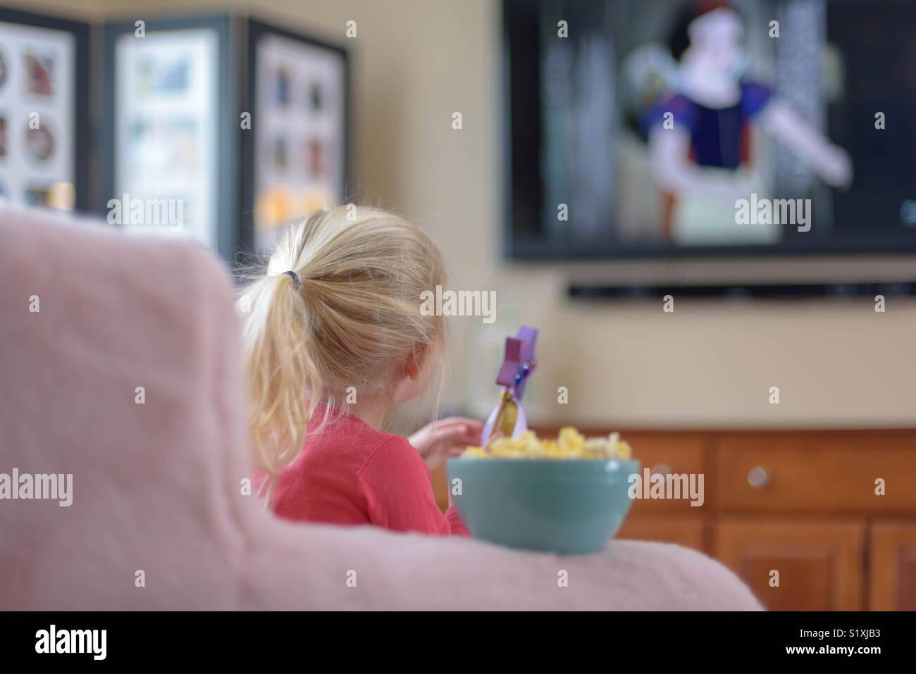 Vue de l'arrière petite fille de regarder un film à la télévision avec un bol de maïs soufflé Banque D'Images