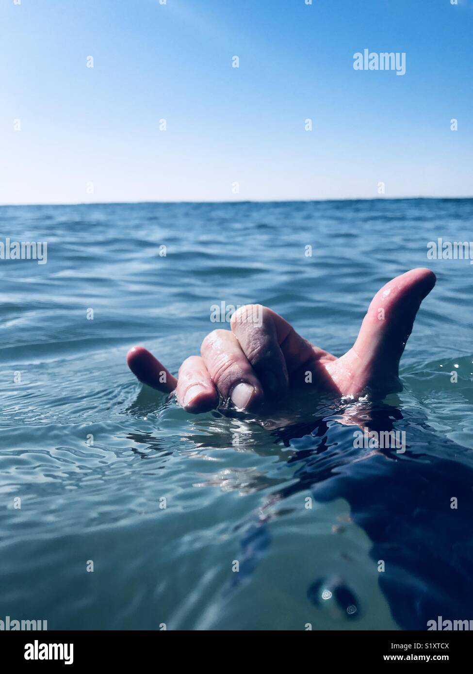 Une main dans l'eau donnant l'pendre signe ou le Shaka. Banque D'Images