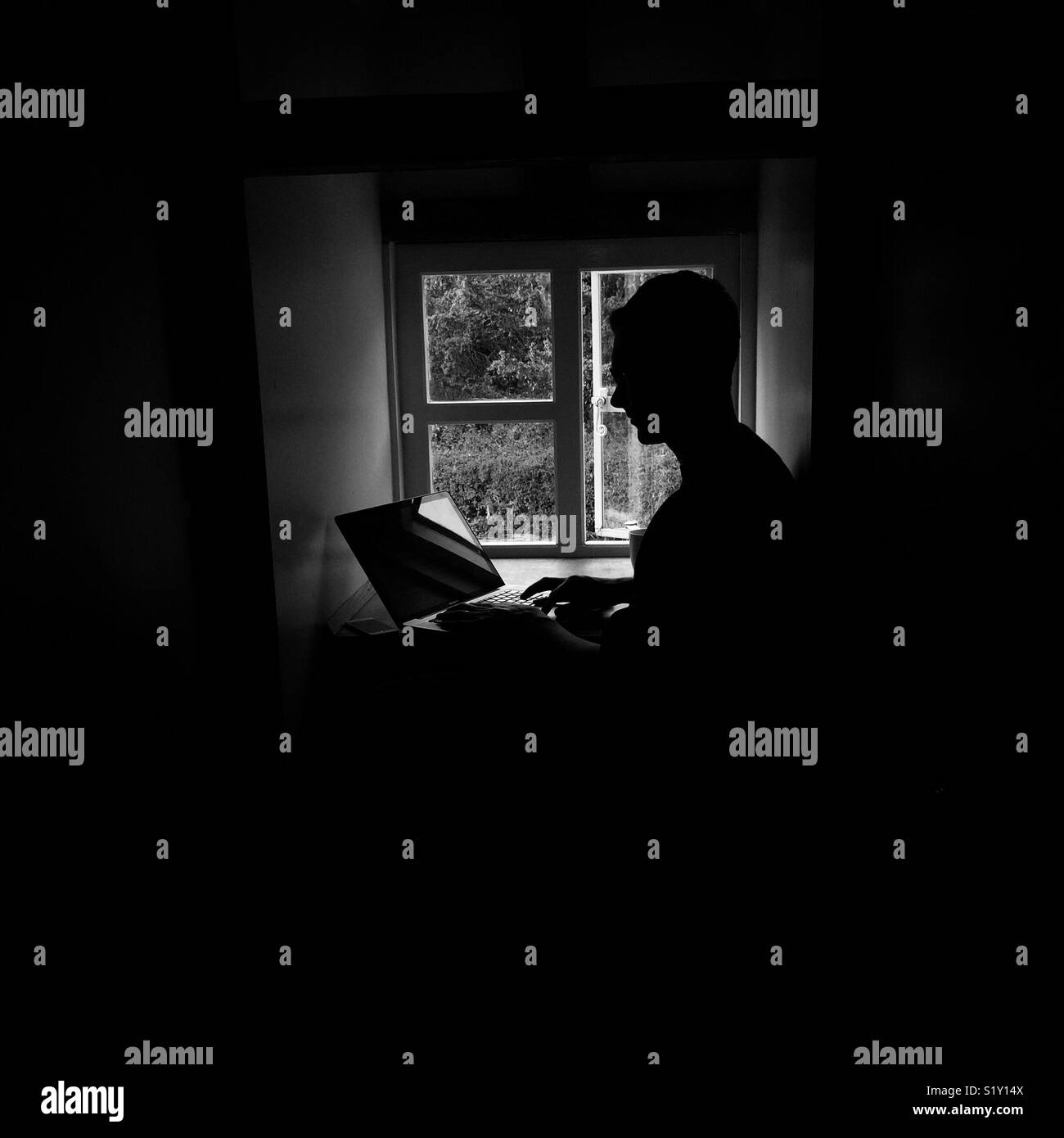 L'homme silhouette sur une fenêtre à l'aide d'un ordinateur portable. Banque D'Images