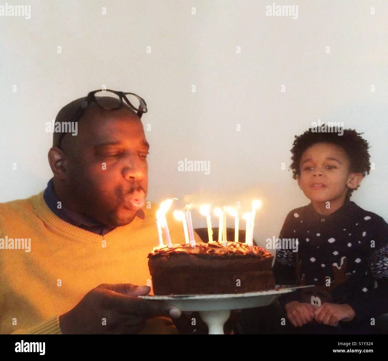 Père blowing out candles sur un gâteau d'anniversaire. - Image de stock capturée avec un smartphone