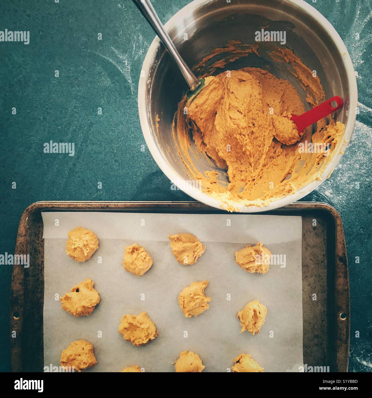 Faire des cookies à la citrouille vue plate en acier inoxydable montrant bol plein de pâte à biscuits de papier parchemin et plateau avec cookie cuillerées de pâte Banque D'Images