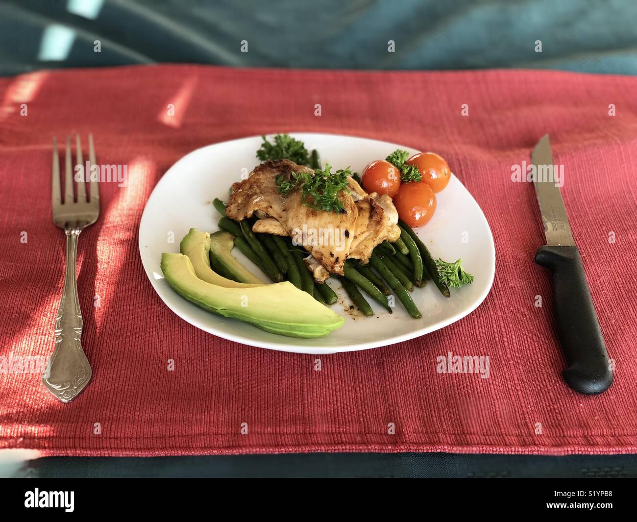 Dîner pour une : citron, la moutarde de Dijon et aux herbes poulet mariné garnie de persil frisé sur lit de haricots verts, avec des tomates cerises et de l'avocat Banque D'Images