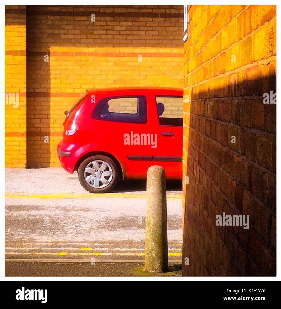 Petite voiture rouge garée dans un environnement urbain avec mur de brique en premier plan. Banque D'Images