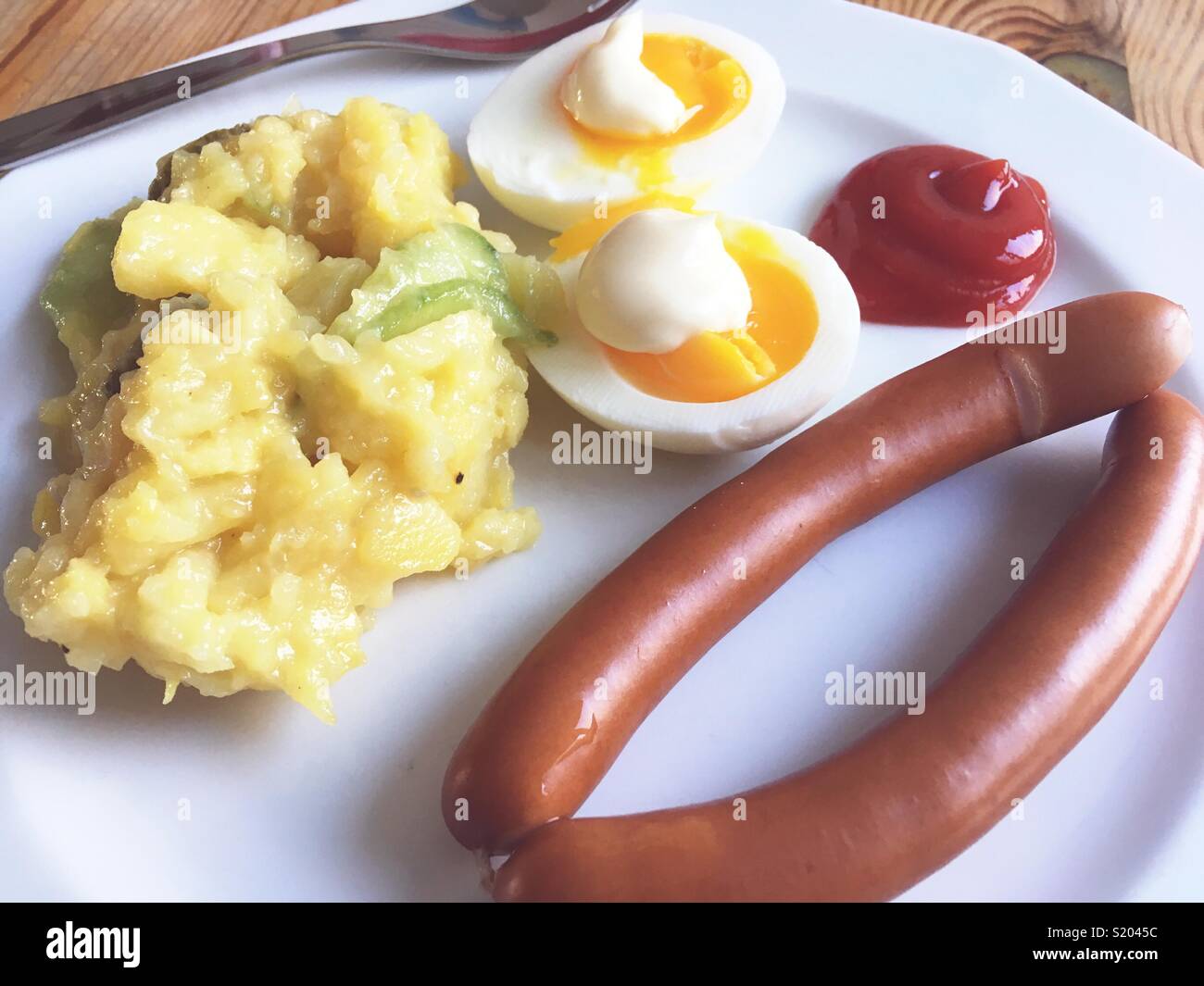 Une paire de saucisses de Vienne, oeufs, mayonnaise, ketchup et salade de pommes de terre sur une plaque blanche Banque D'Images
