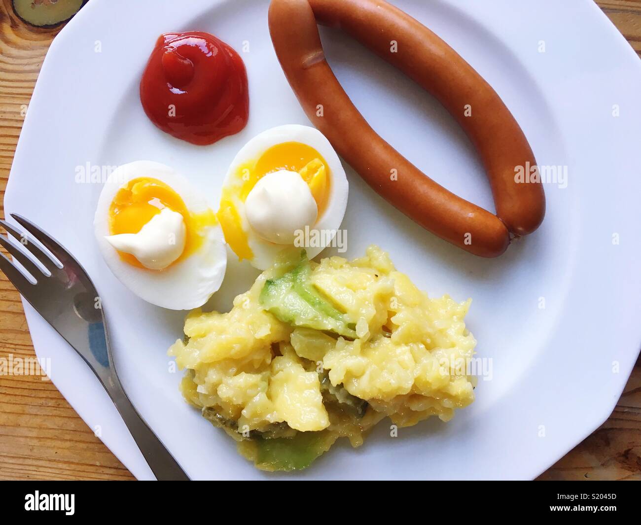 Une paire de saucisses de Vienne, oeufs, mayonnaise, ketchup et salade de pommes de terre sur une plaque blanche Banque D'Images