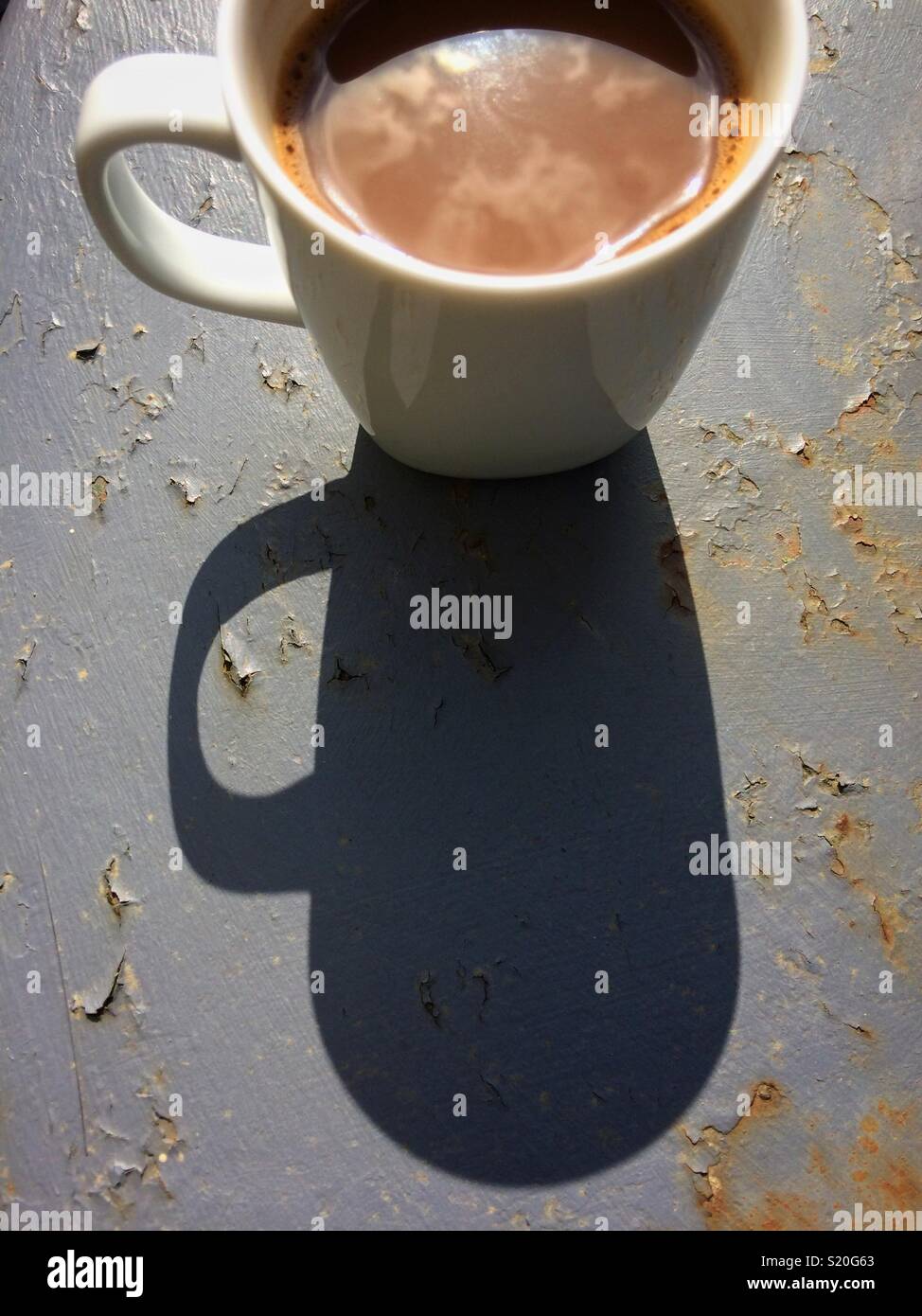 Tasse de café dans le soleil du matin avec une grande ombre sur une table de jardin en métal gris Banque D'Images