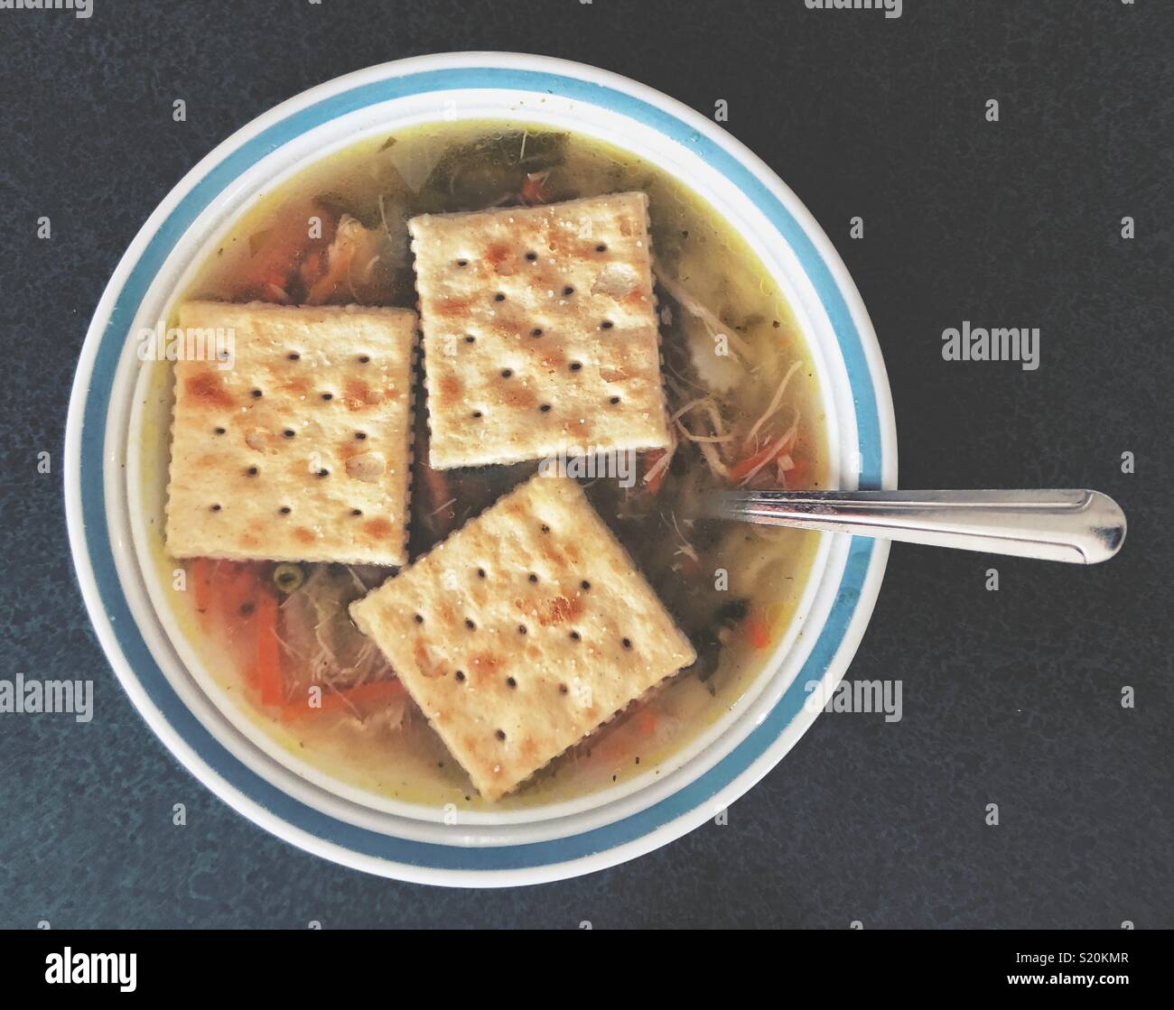 Mise à plat sur bol de soupe au poulet fait maison avec trois saltine crackers flottant sur top - Image de stock capturée avec un smartphone