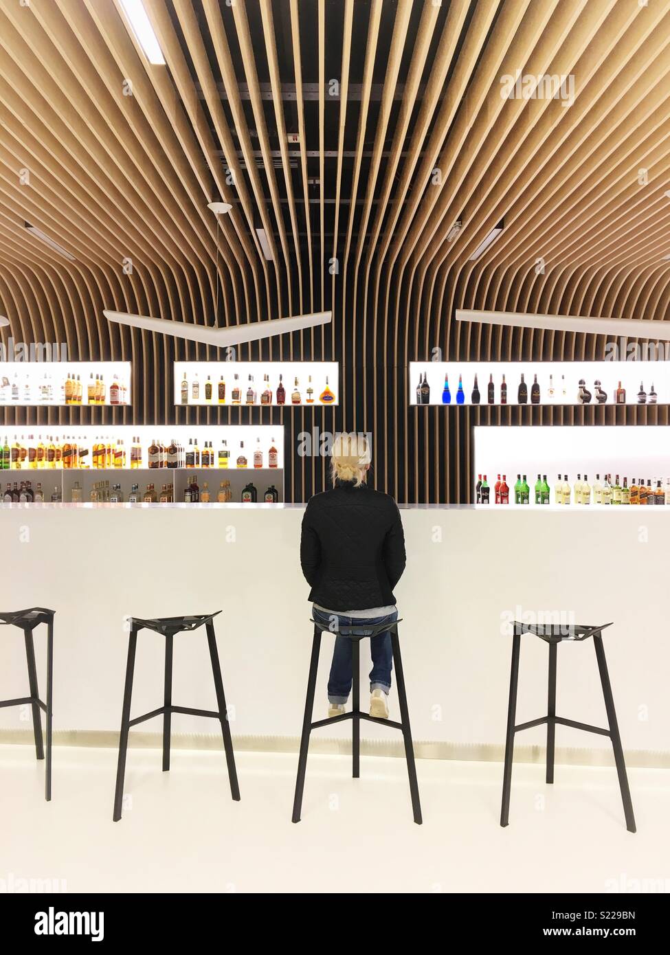 Une femme assise sur une chaise en face d'un bar pour prendre un verre seul d'attente Banque D'Images