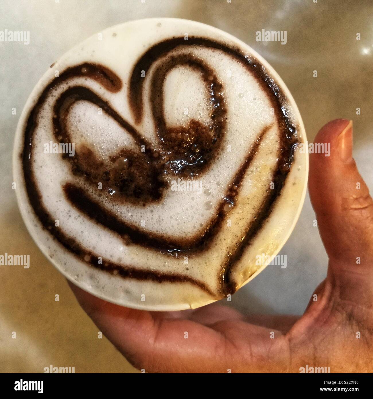 Femme tenant un café blanc mousseux avec un smiley coeur dans une tasse à emporter Banque D'Images