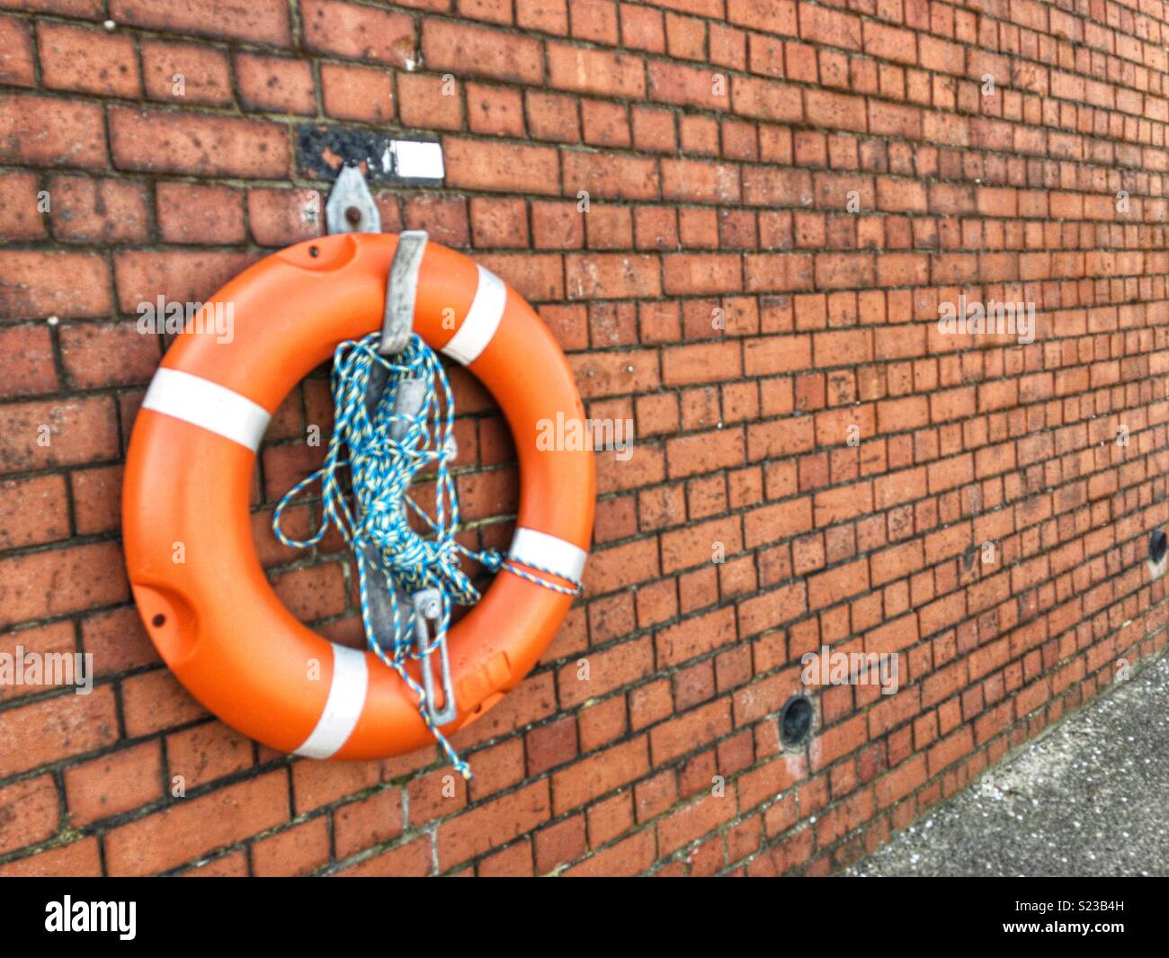 Bouée Orange avec corde bleu et blanc, monté sur un mur de briques par la rivière Mersey, Wallasey, Wirral, Angleterre Banque D'Images