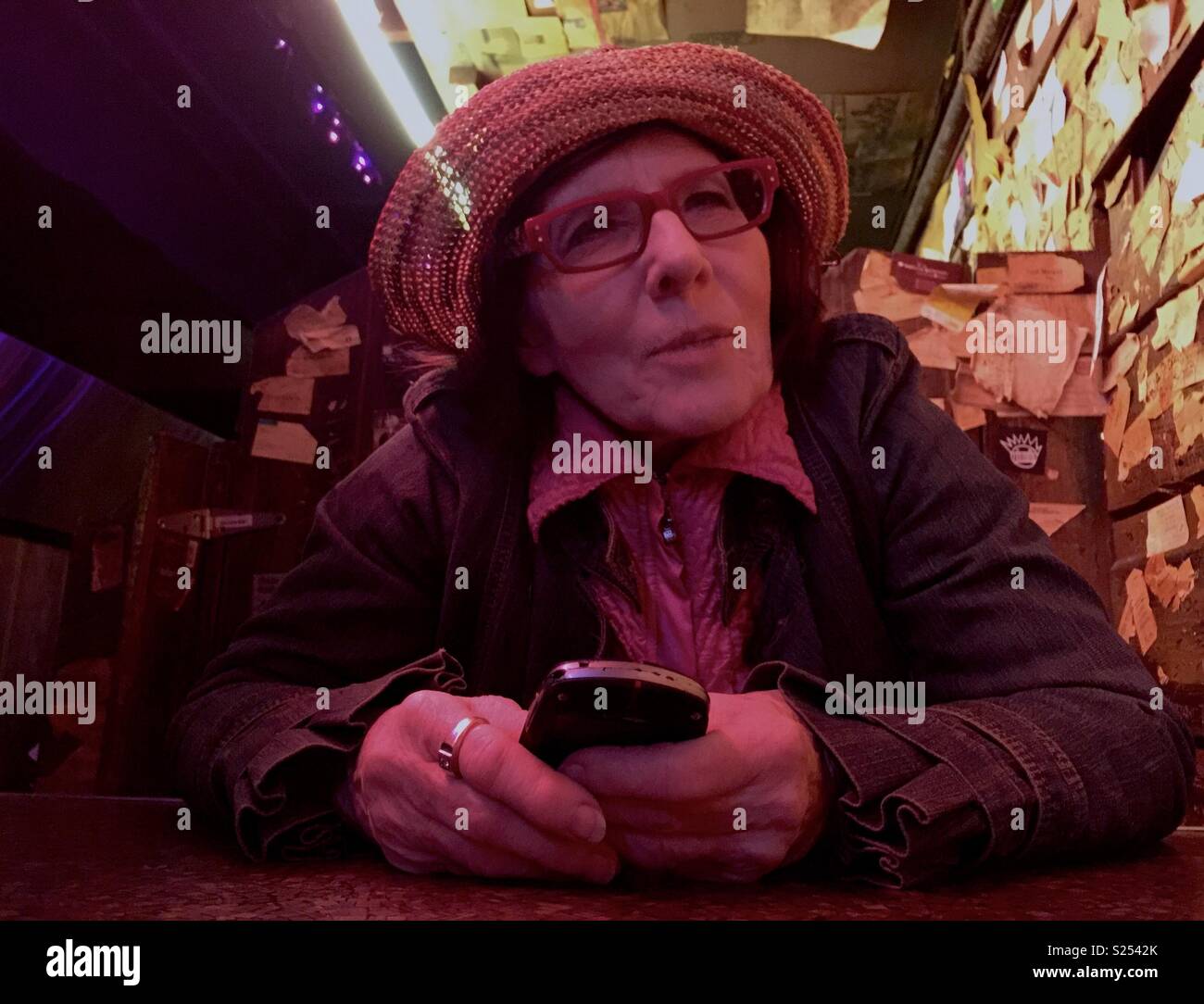Femme âgée de la hanche dans un bar dans un chapeau avec un cellulaire. Banque D'Images