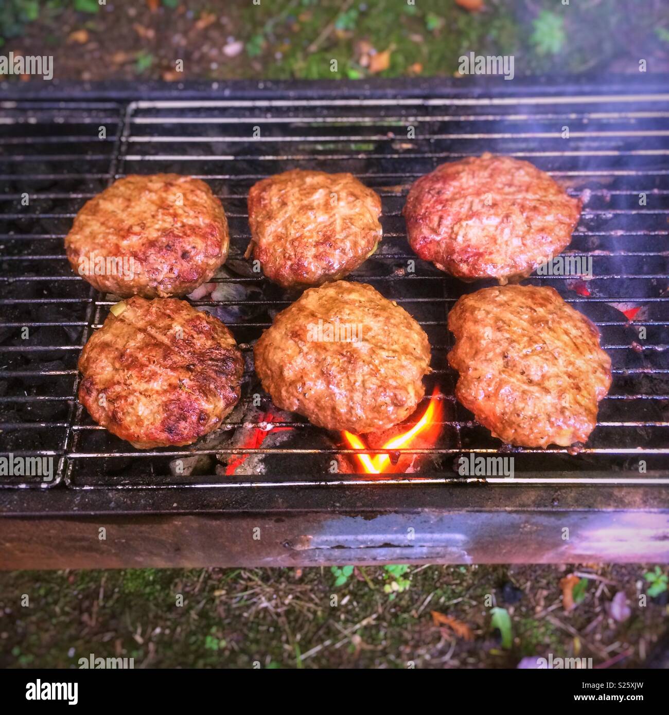 La cuisson des hamburgers faits maison sur un barbecue au charbon, Hampshire, Angleterre, Royaume-Uni. - Image de stock capturée avec un smartphone