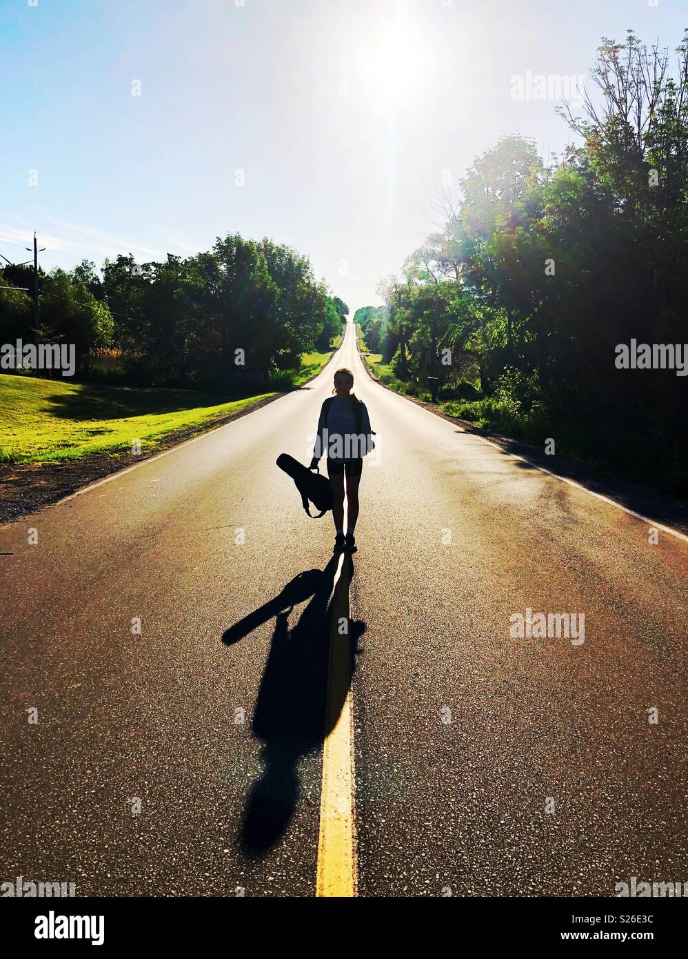 Silhouette et ombre de teen girl holding ukulele en position debout au milieu de la route au lever du soleil Banque D'Images