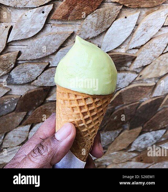 Main tenant cornet gaufré vert lime de l'avocat et la crème glacée contre un arrière-plan bois Banque D'Images