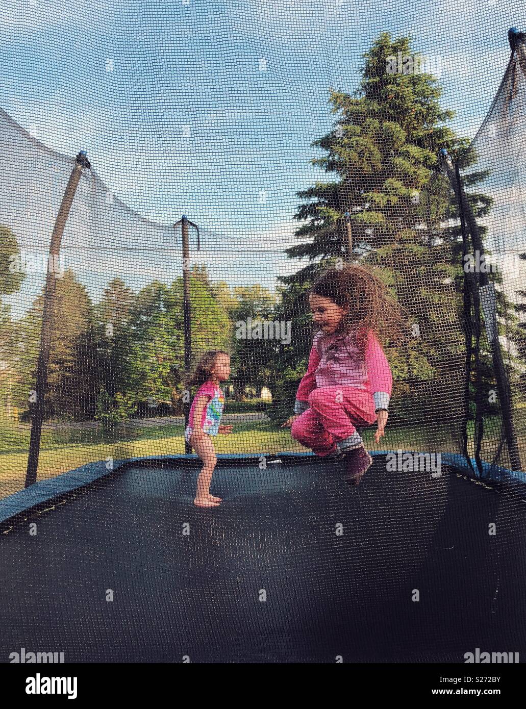 Deux jeunes filles sautant sur un trampoline en pyjama avec une en plein vol. Banque D'Images