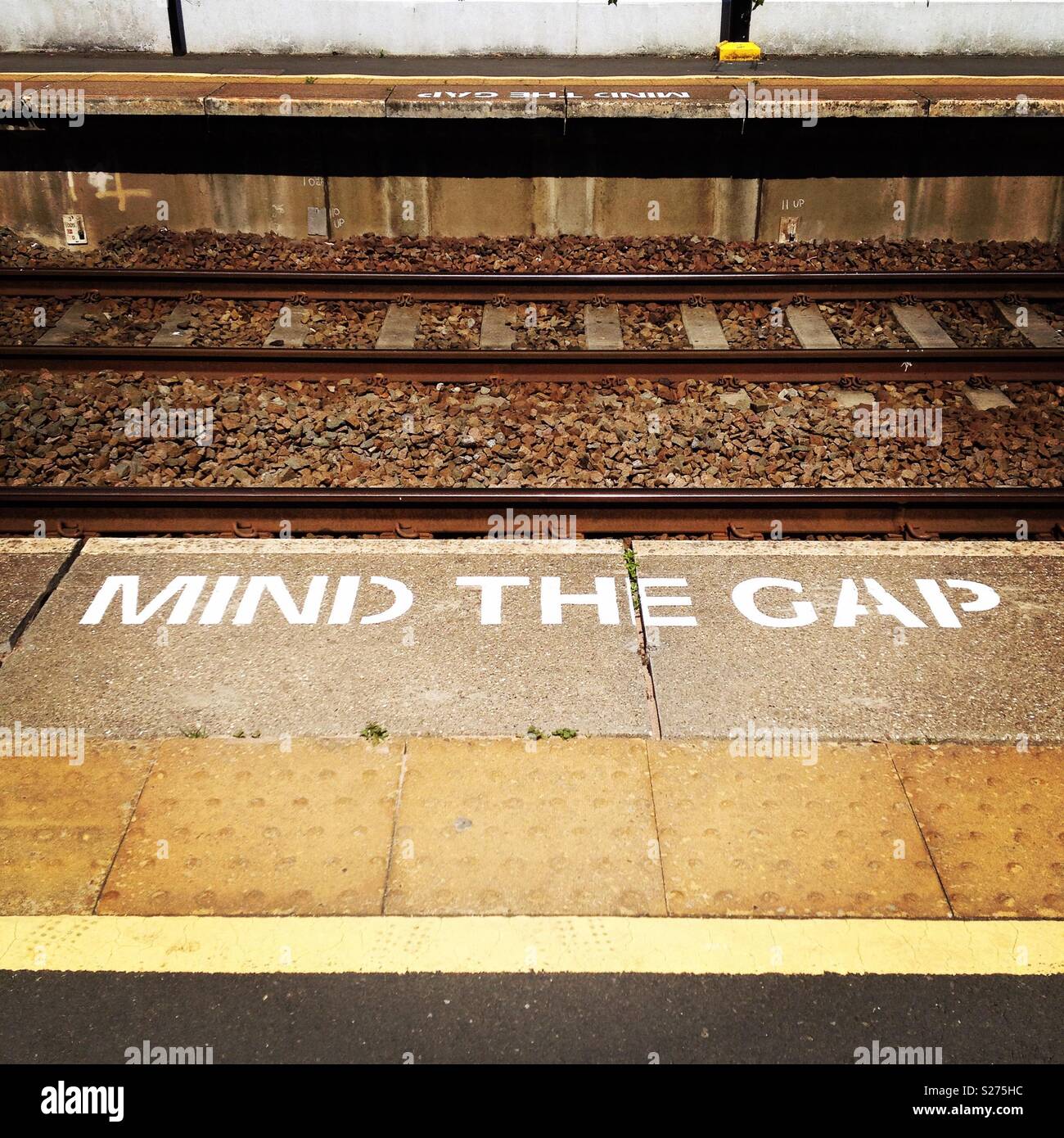 'Mind l'écart' signe peint en blanc sur le bord de la plate-forme ferroviaire Banque D'Images