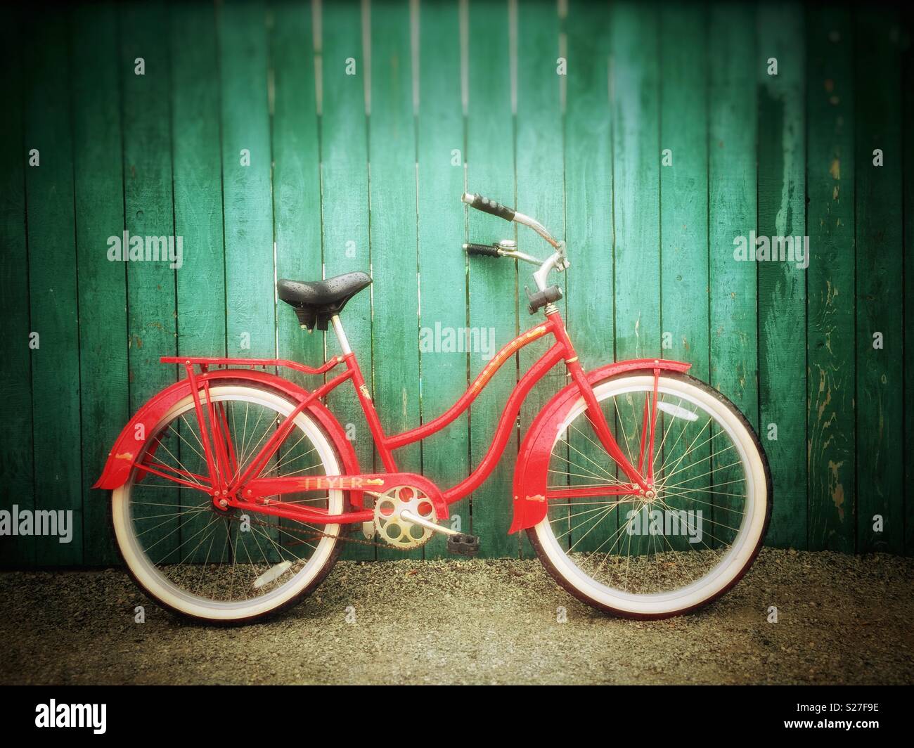 Vintage red Flyer location avec pneus blanc appuyé contre une clôture de bois vert sur un chemin de gravier. - Image de stock capturée avec un smartphone