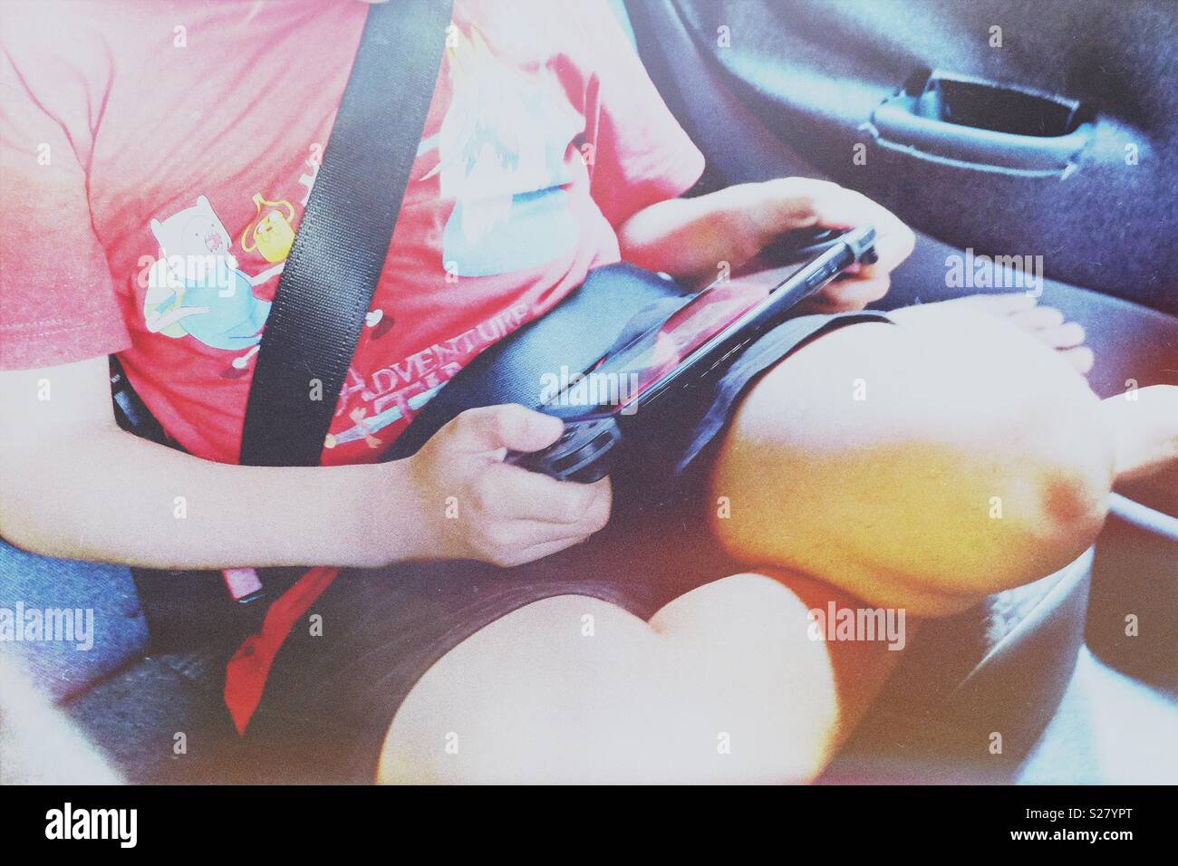 Un garçon dans un le siège arrière d'une voiture de jouer à un jeu sur une console Banque D'Images