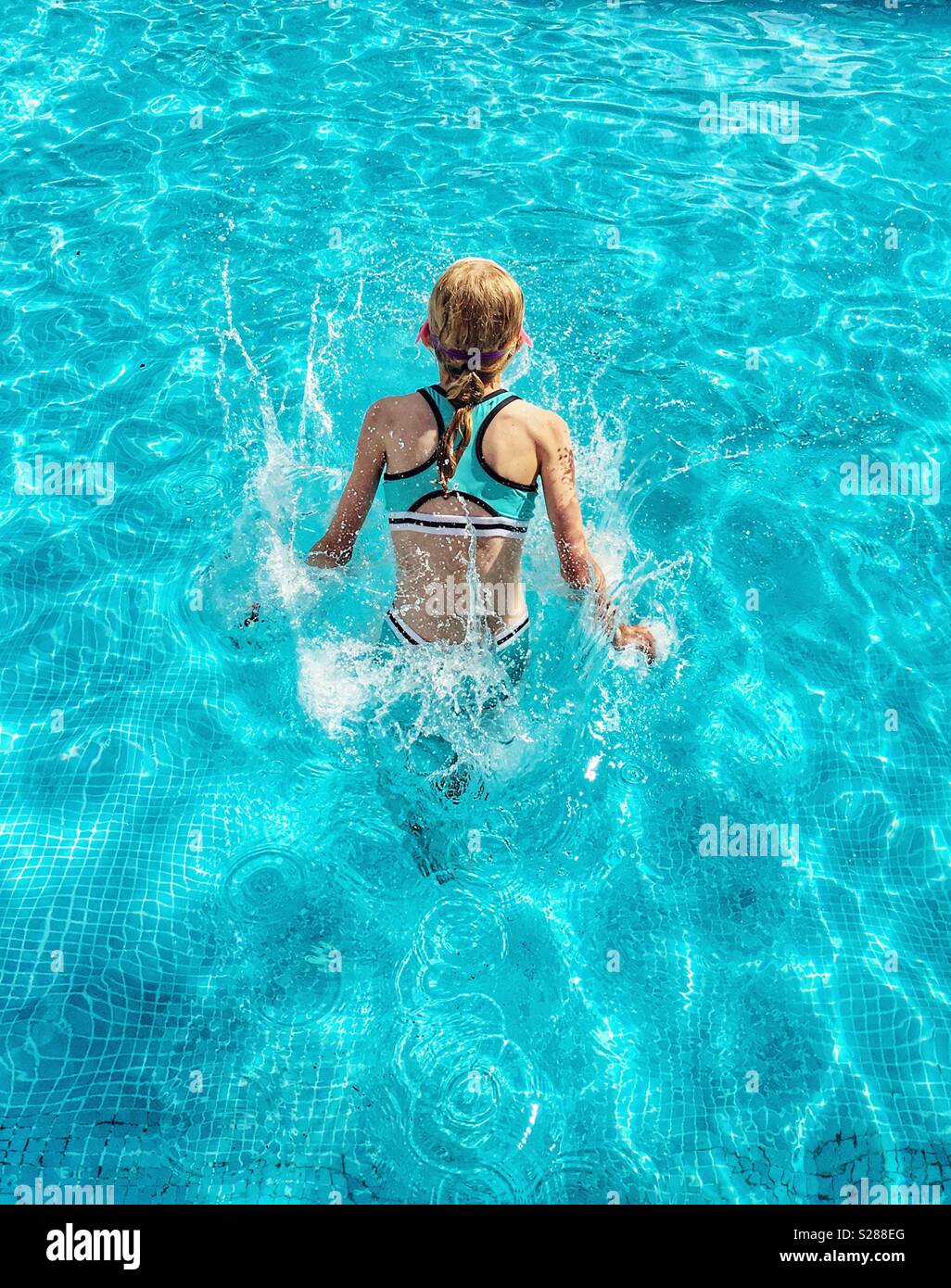 Jeune fille en bleu maillot de la projection dans le bleu piscine Banque D'Images