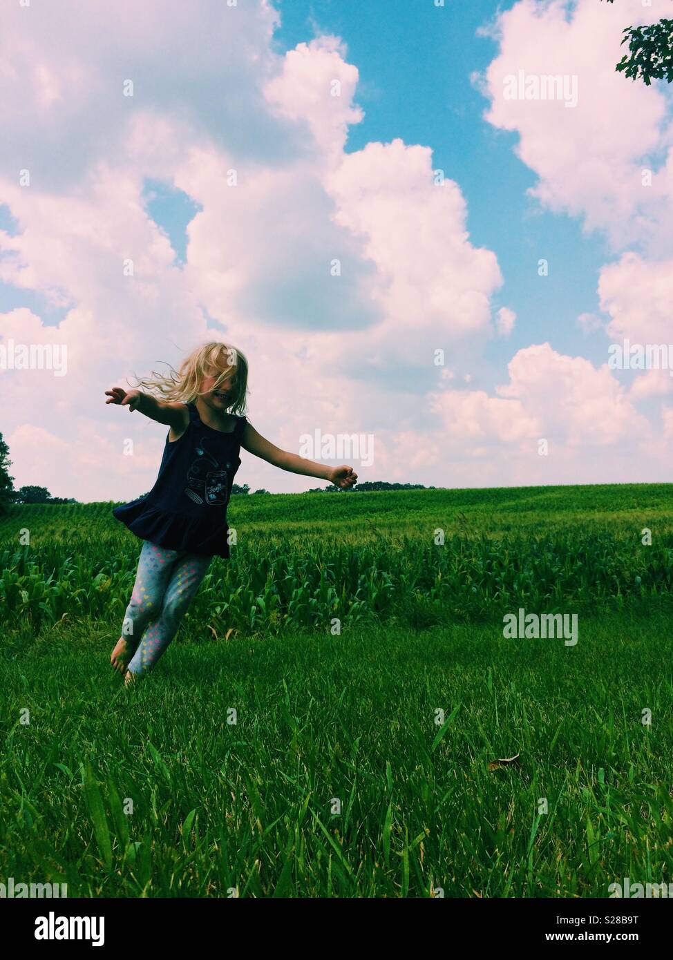 Jeune fille virevoltant dans champ vert avec ciel bleu au-dessus Banque D'Images