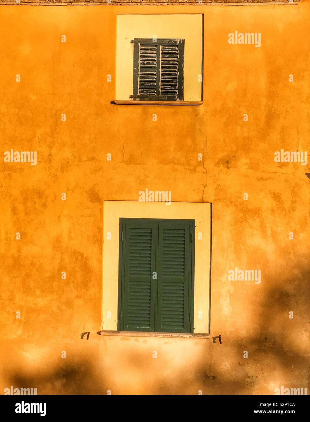 Les petites et grandes fenêtres aux volets verts dans mur de plâtre jaune Banque D'Images