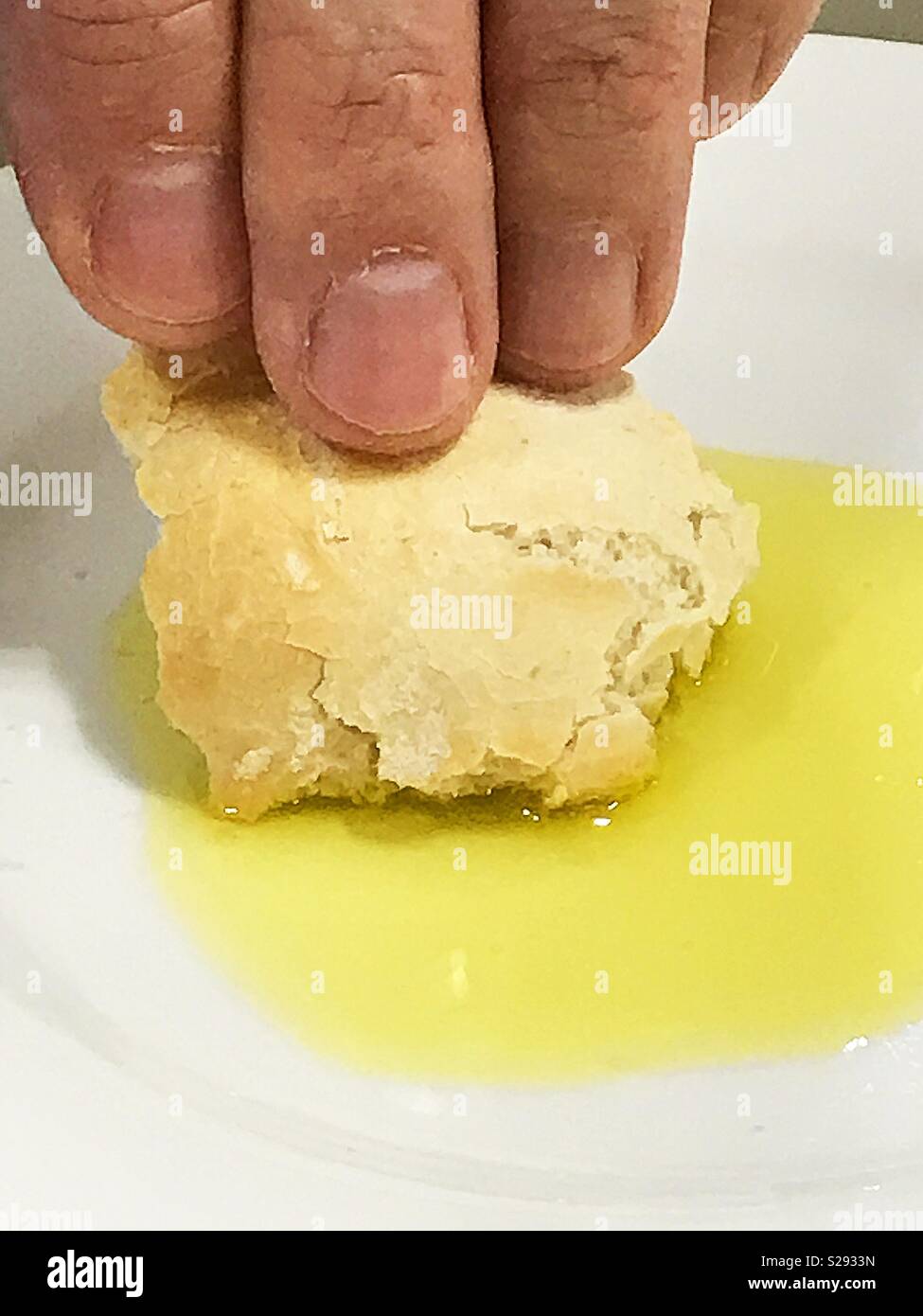 La main de l'homme trempant du pain dans l'huile d'olive. - Image de stock capturée avec un smartphone