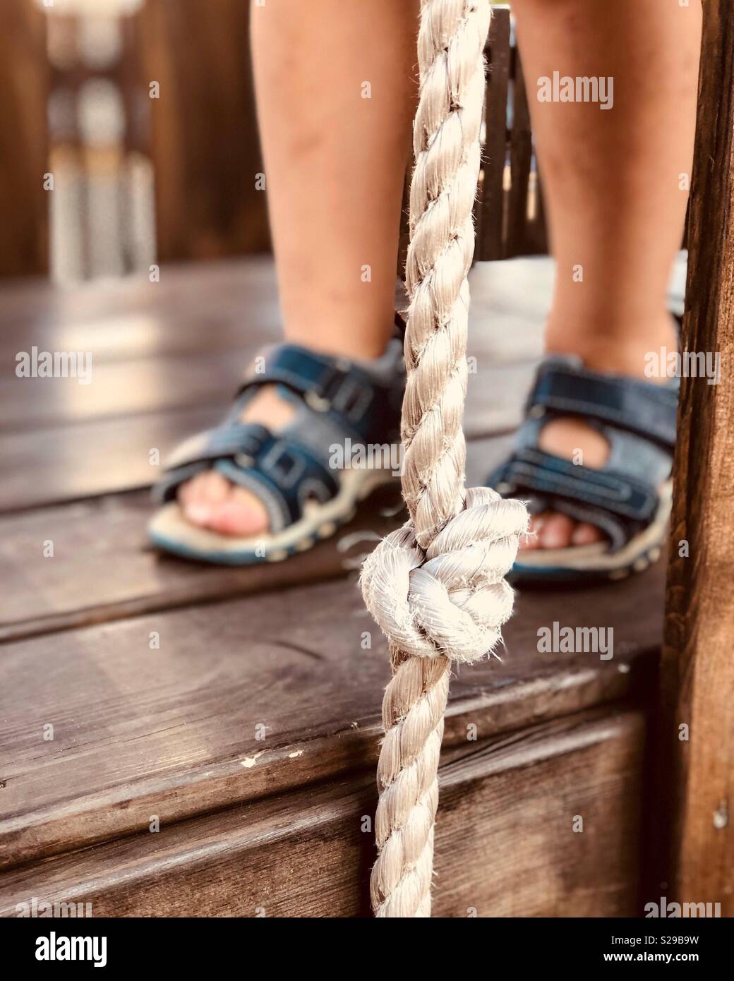 Tout-petit'pieds en sandales bleu sur une terrasse en bois avec une corde blanche Banque D'Images