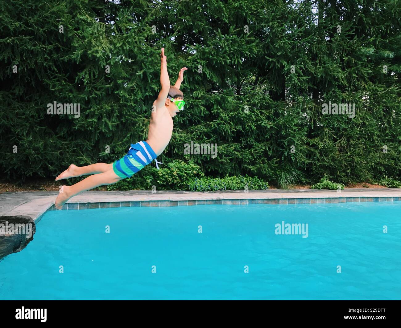 Un jeune garçon sautant dans une piscine extérieure en été. Banque D'Images