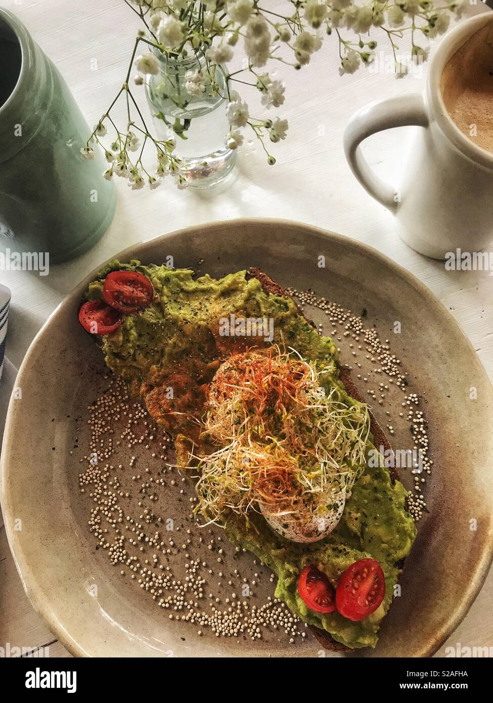 Toast à l'avocat avec les oeufs pochés, les germes de luzerne et les tomates et du cappuccino, plaqué avec petit-déjeuner Banque D'Images