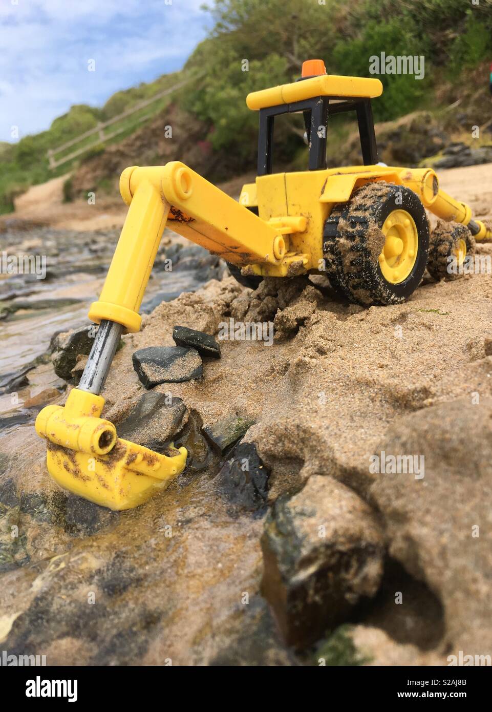 L'enfant digger toy posées dans le sable et l'eau sur une plage à regarder en pleine dimension en utilisant la technique de perspective forcée. Rock beach, Cornwall. Banque D'Images