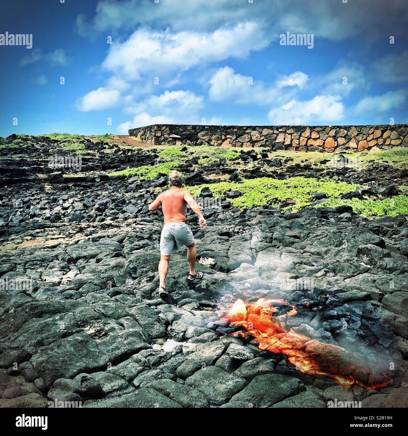 Homme qui court jusqu'à la colline avec éruption de lave en fusion à Hawaii sous un ciel bleu nuageux partiellement Banque D'Images