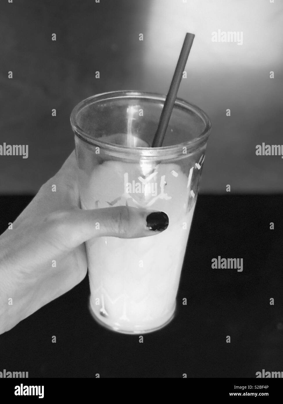 Le noir et blanc photo d'une main de femme tenant un verre de lait avec une paille Banque D'Images