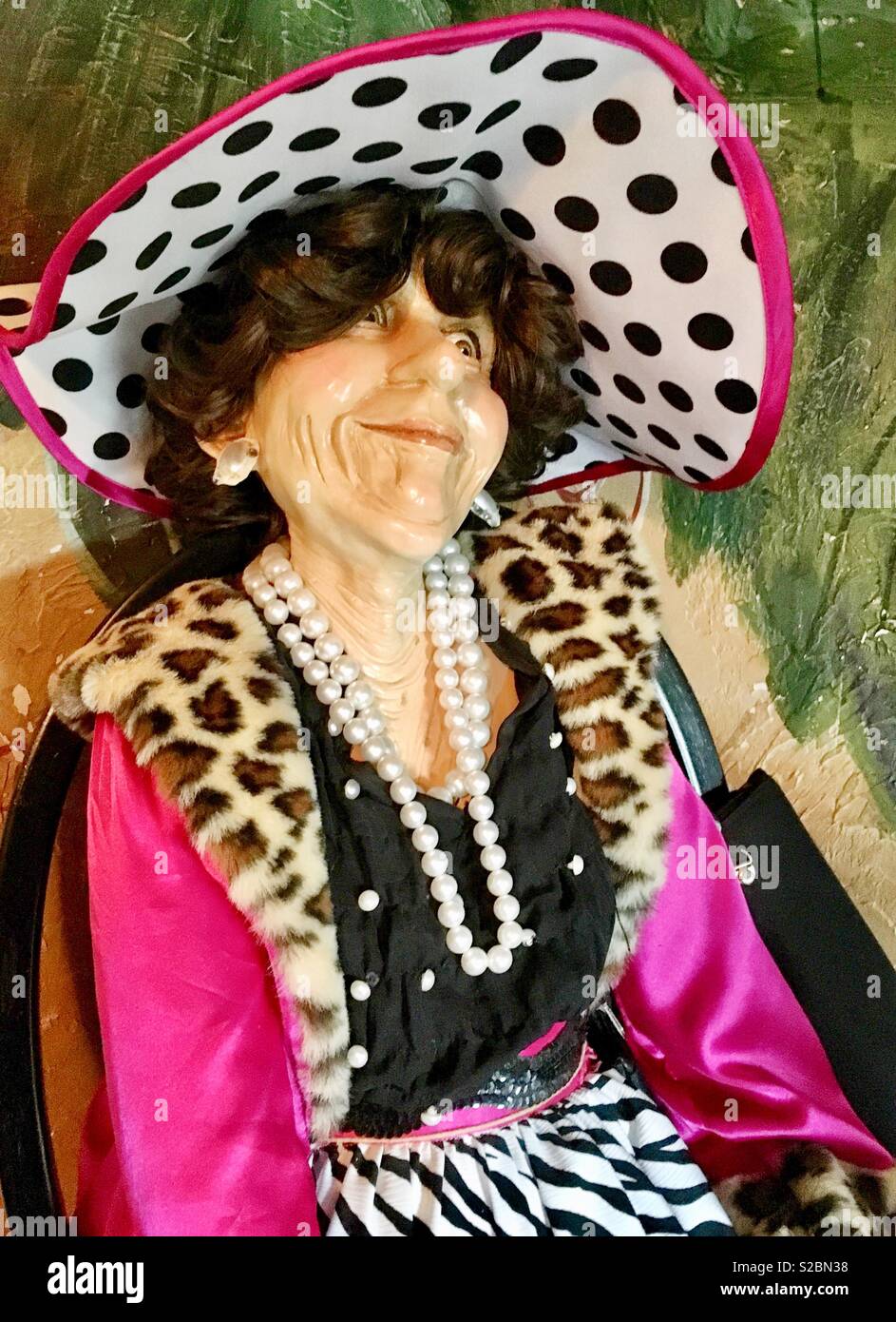 Mannequin d'une femme âgée assise dans un fauteuil avec noir sac à main noir vêtu de noir et blanc à pois rose avec chapeau, manteau rose en fausse fourrure léopard, pearl strands, chemisier noir jupe imprimée zèbre Banque D'Images