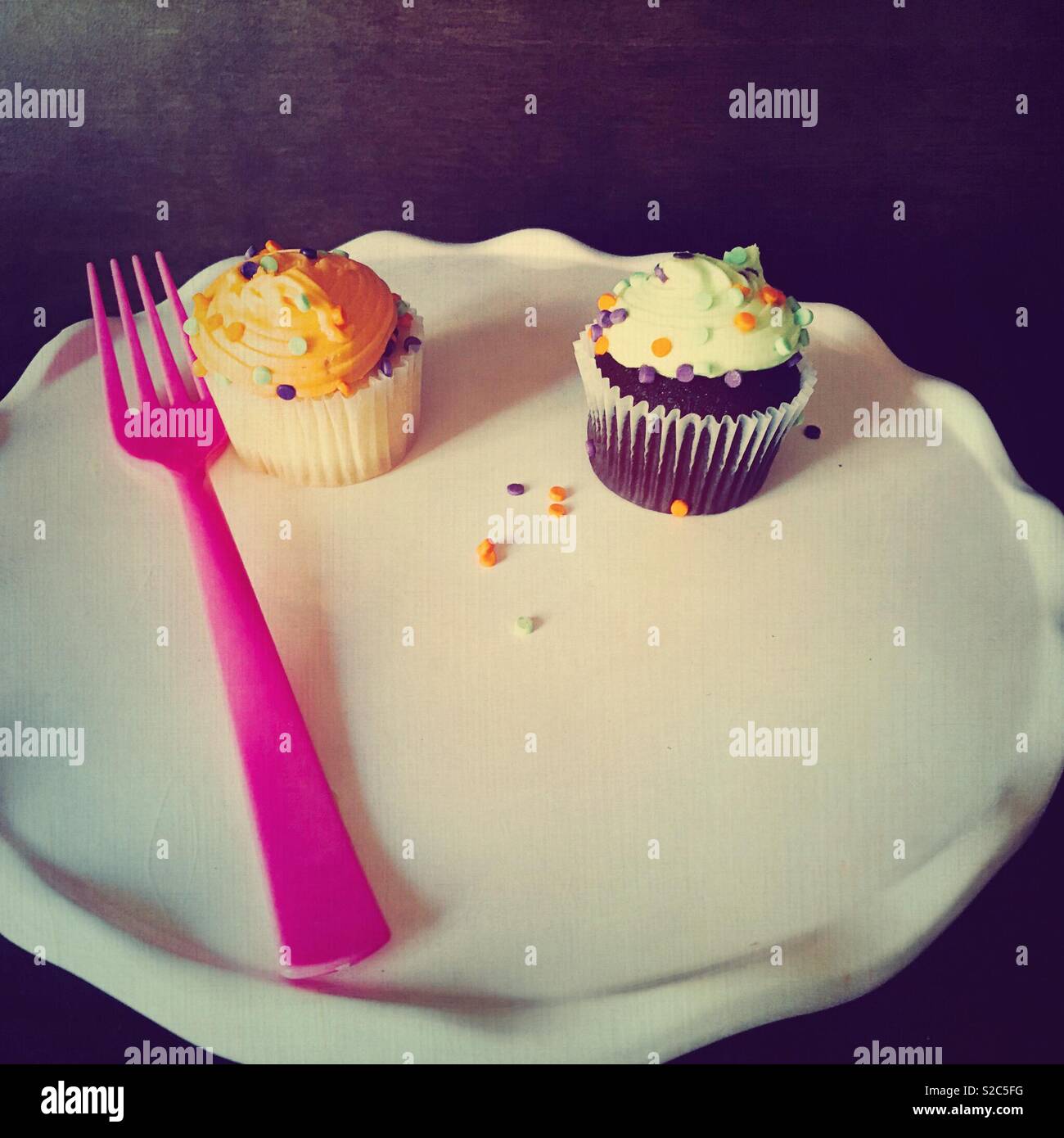 Vanille et chocolat colorés cupcakes avec le glaçage et saupoudre servi sur une plaque blanche avec un tablier rose Banque D'Images
