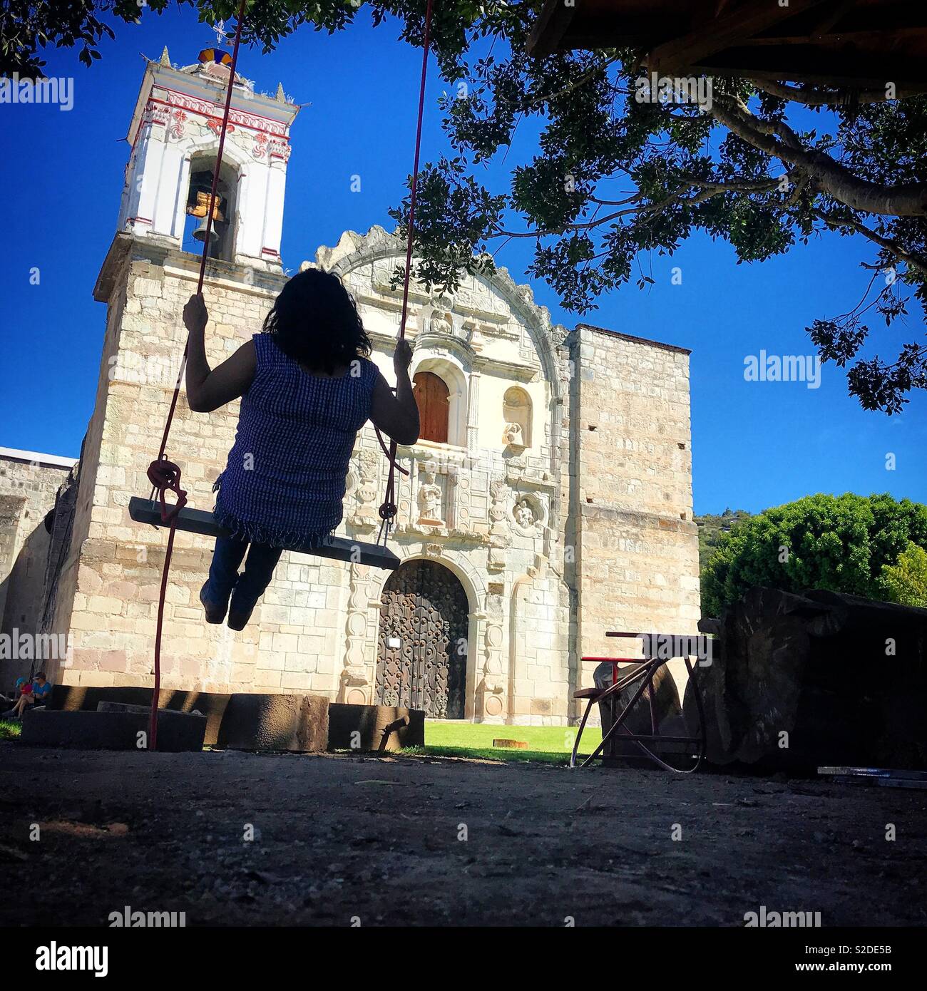 Une femme assise sur une balançoire en face de l'église de Lachatao, dans la Sierra Norte de Oaxaca, Mexique Banque D'Images