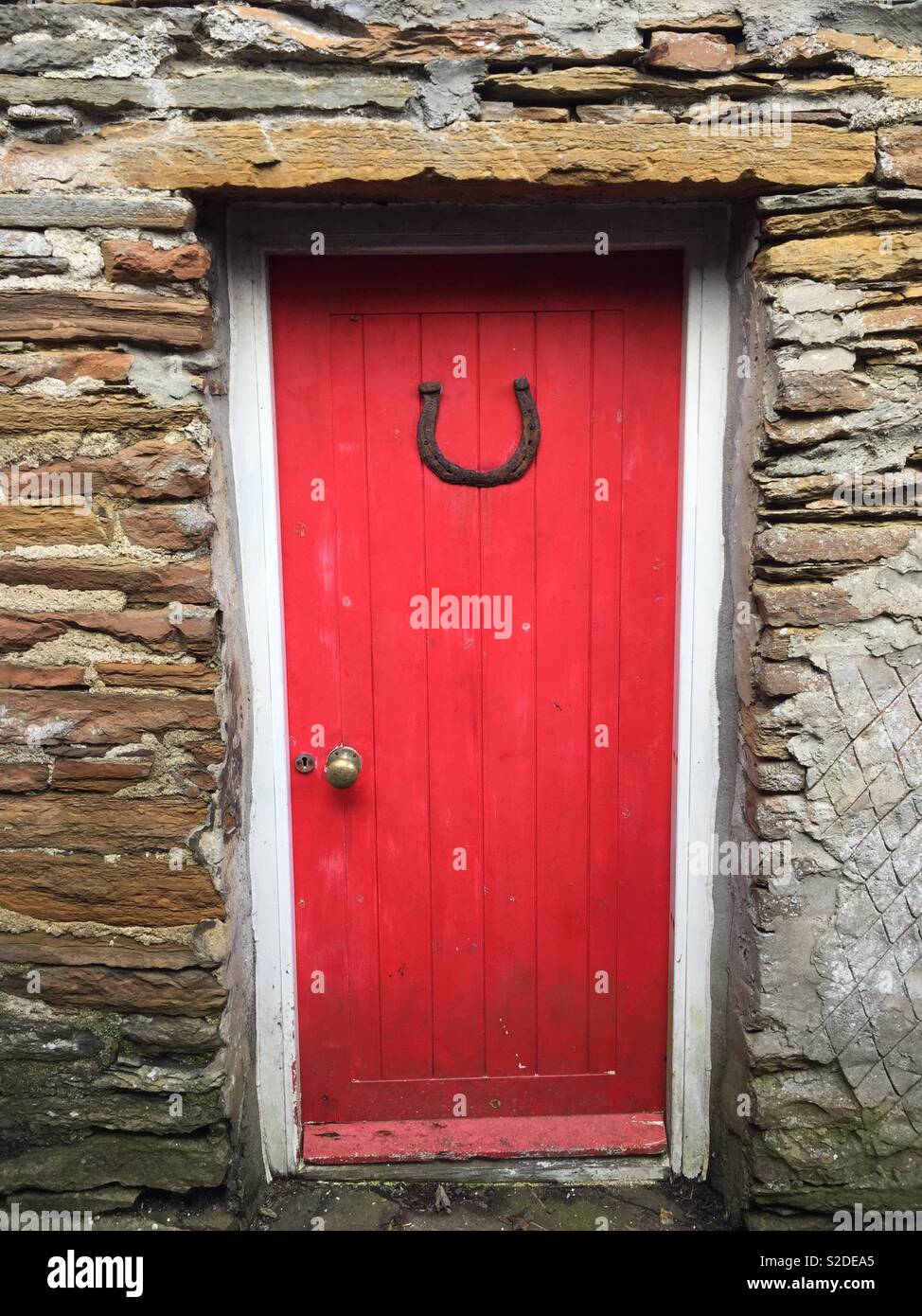 Bonne chance - Rouge porte dans mur en pierre chambre avec lucky horseshoe, Stromness, Orkney Banque D'Images